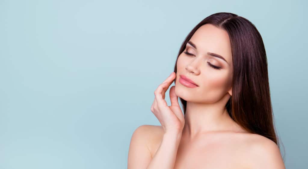 Woman touching her cheek while showcasing a slim, contoured facial profile after buccal fat reduction