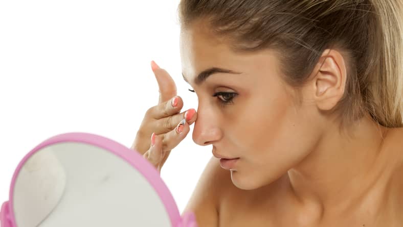 woman looking at her nose in the mirror after rhinoplasty